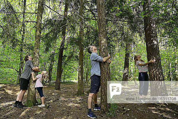 Parents and children embracing tree while standing in forest