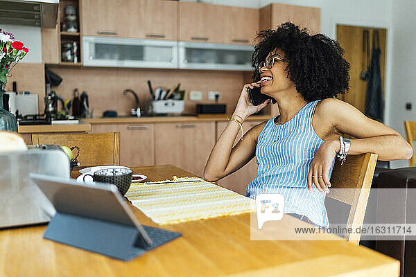 Fröhliche junge Frau  die sich über ihr Smartphone unterhält  während sie im Home Office arbeitet
