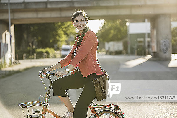 Lächelnde junge Frau fährt Fahrrad auf der Straße in der Stadt