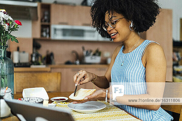 Junge Frau mit lockigem Haar  die zu Hause Brot auf dem Tisch buttert