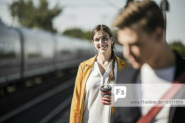 Smiling young woman with reusable coffee mug at railroad station