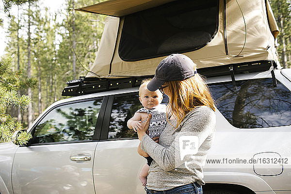 Frau hält kleinen Sohn (6-11 Monate) auf Camping  Auto mit Zelt im Hintergrund  Wasatch Cache National Forest