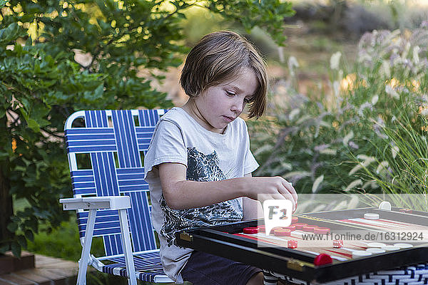 Ein kleiner Junge spielt Backgammon im Freien in einem Garten.