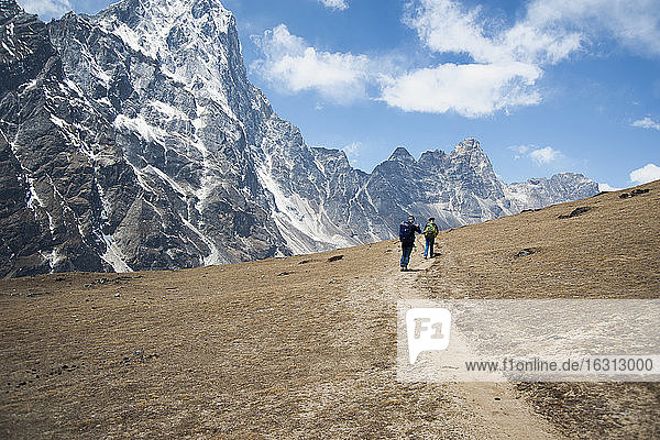 Zwei Bergsteiger auf einem Pfad mit Blick auf die steilen Berge.