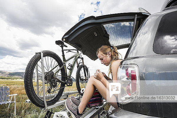Teenage girl sitting on the tailgate of an SUV looking at vista