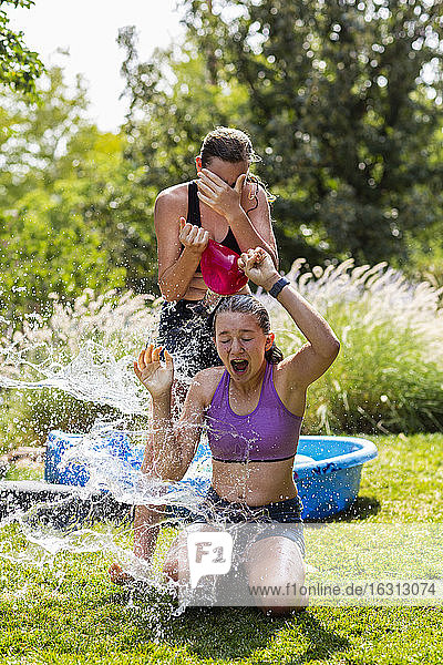Zwei Mädchen im Teenageralter in Badeanzügen spielen in einem Garten mit Wasserballons.