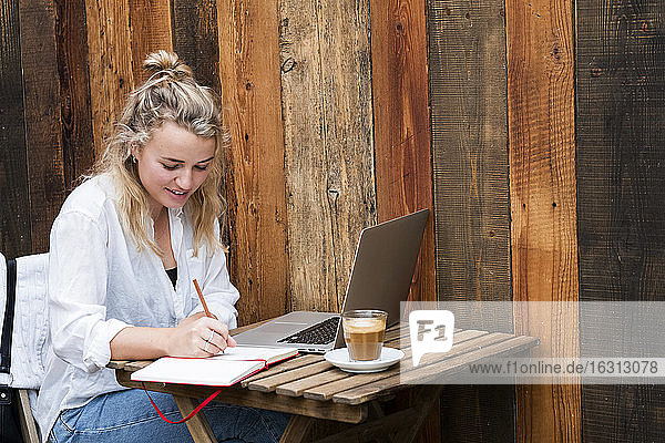 Young blond woman sitting alone at a cafe table with a laptop computer  working remotely.