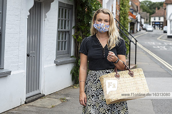 Young blond woman wearing face mask walking through village  carrying shopping bag.
