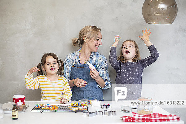 Blond woman wearing blue apron and two girls baking Christmas cookies.