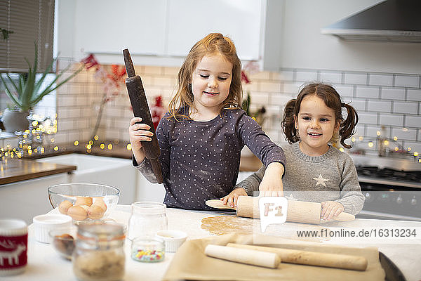 Two girls standing in kitchen  baking Christmas cookies.