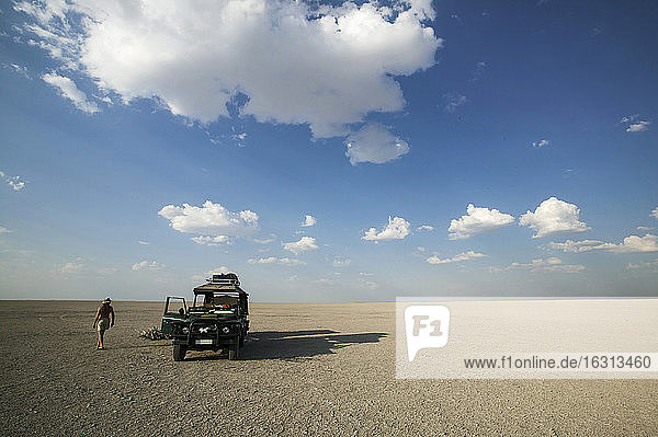 Man walking past 4x4 parked on the Makadikadi Salt Pans in Botswana.