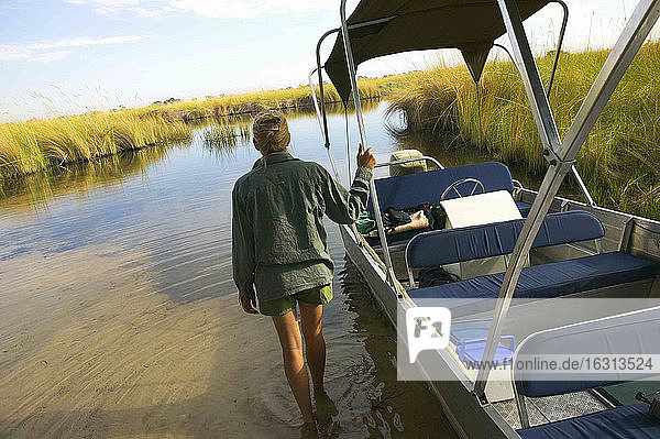 Rückansicht einer im Wasser watenden Frau  schiebendes Boot  Okavango-Delta  Botswana.