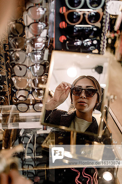 Reflexion einer selbstbewussten Frau  die eine Sonnenbrille im Spiegel im Modegeschäft anprobiert