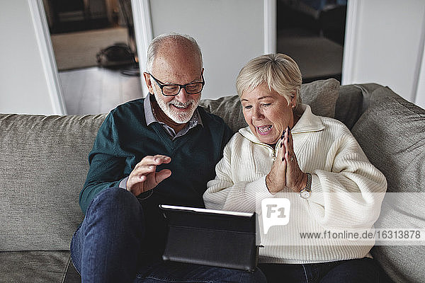 Lächelndes älteres Ehepaar benutzt digitales Tablet  während es auf dem Sofa im Wohnzimmer sitzt