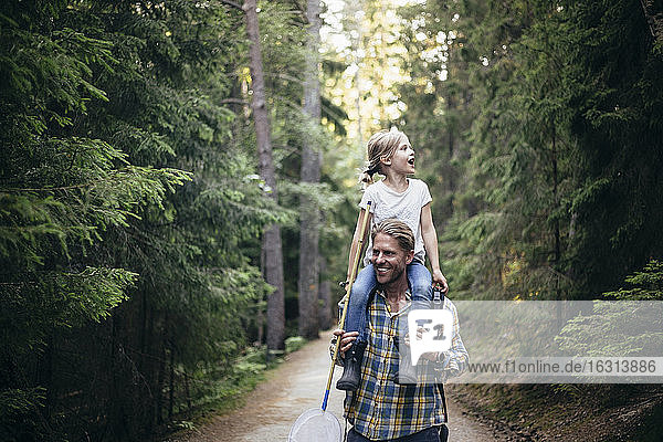 Lächelnder Vater trägt Tochter auf der Schulter beim Waldspaziergang