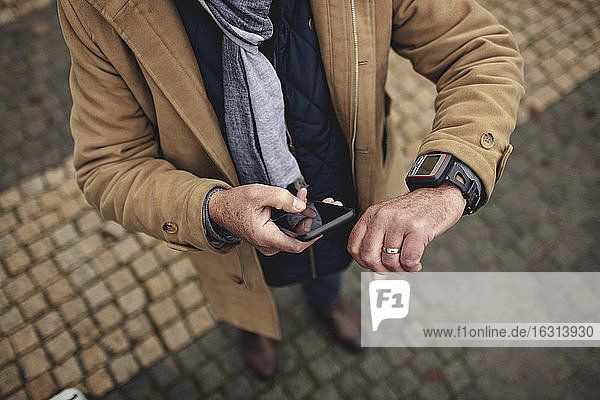 Niedrigerer Teil des Mannes benutzt Telefon  während er auf dem Fußweg die Zeit überprüft