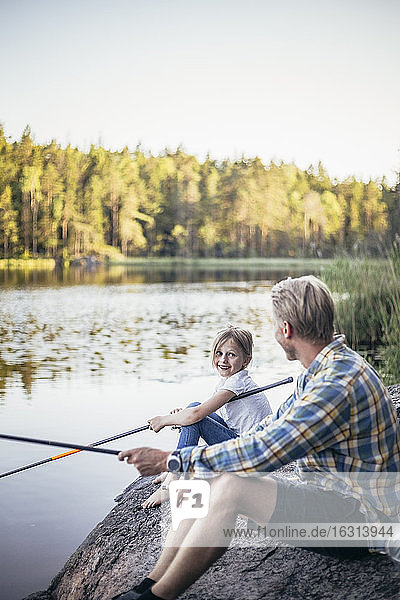 Smiling daughter looking at father while fishing at lake