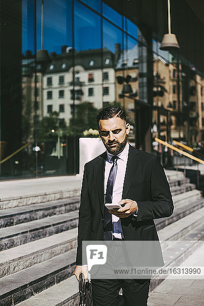Businessman using smart phone while walking in city