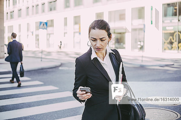 Geschäftsfrau betrachtet Smartphone beim Überqueren einer Straße in der Stadt