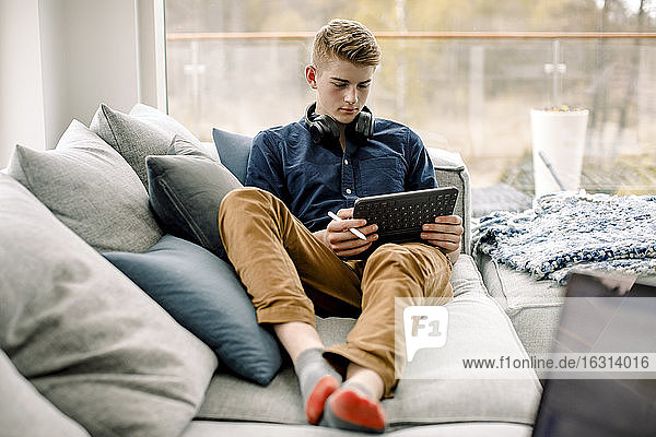 Teenager benutzt digitales Tablet  während er zu Hause auf dem Sofa sitzt