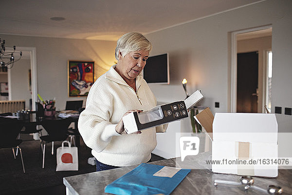 Zerknitterte ältere Frau packt Kiste über Kücheninsel aus