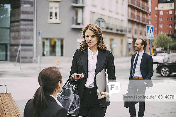 Female entrepreneurs communicating while coworker standing in city