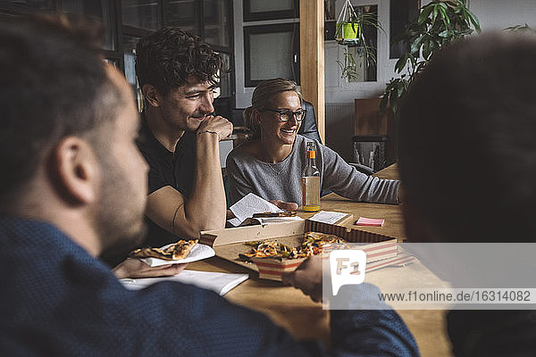 Smiling coworkers eating pizza at workplace