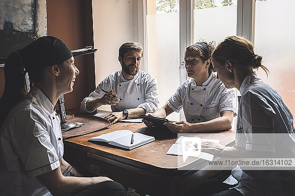 Männliche und weibliche Köche diskutieren  während sie im Restaurant am Tisch sitzen