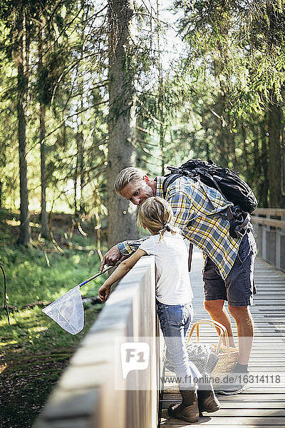 Vater mit Rucksack im Gespräch mit Tochter auf Steg im Wald