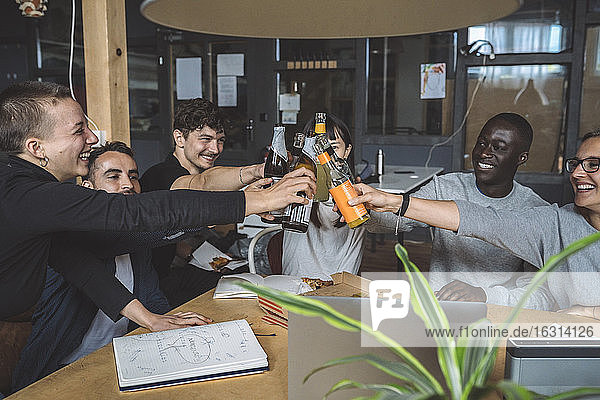 Lächelnde Kollegen stoßen am Arbeitsplatz auf Bier an