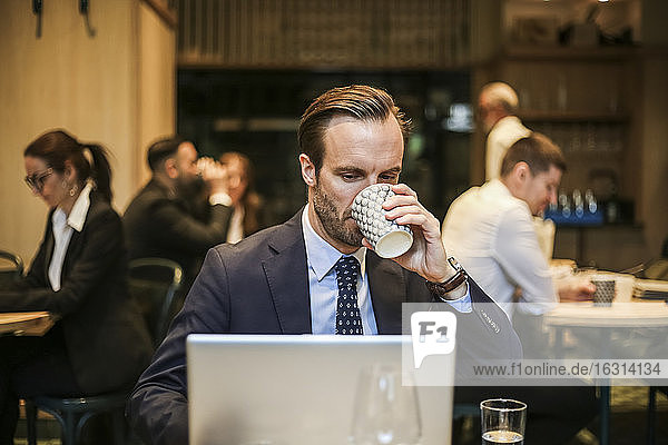 Männlicher Unternehmer arbeitet am Laptop  während er im Restaurant Kaffee trinkt