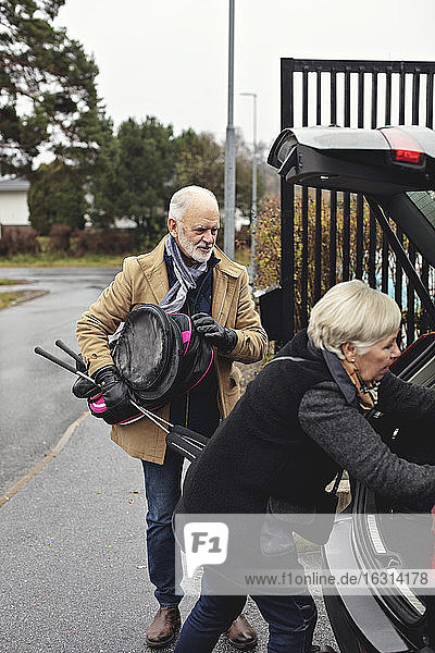 Älterer Mann hält Golfschläger  während der Partner im Winter am Kofferraum des Autos steht