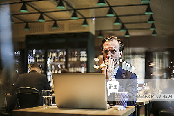 Worried businessman looking at laptop in restaurant