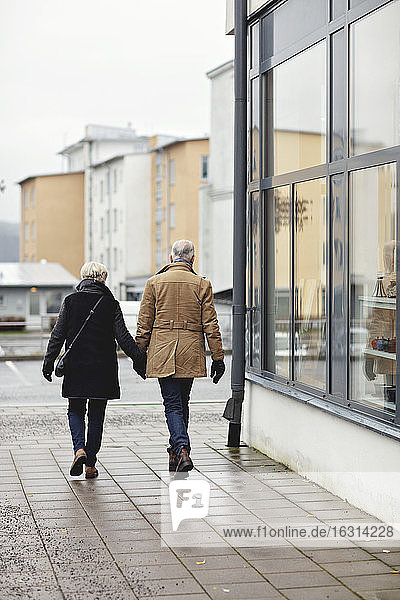 Rückansicht eines älteren Paares  das im Winter beim Gehen auf dem Bürgersteig Händchen hält