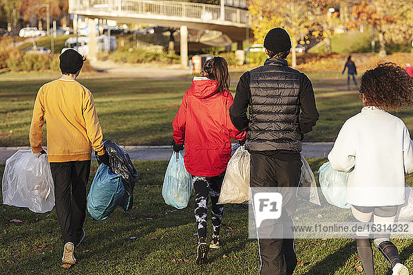 Rückansicht von jungen Umweltschützern  die mit Plastikmüll im Park spazieren