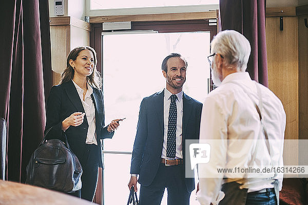 Smiling businesswoman and businessman talking to waiter in restaurant