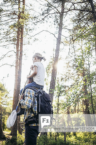 Tiefwinkelansicht eines Vaters  der seine Tochter auf der Schulter im Wald trägt