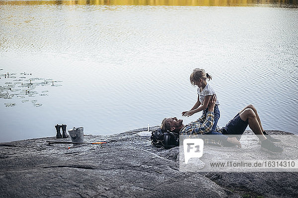 Seitenansicht der Tochter  die auf dem lächelnden Vater am See sitzt