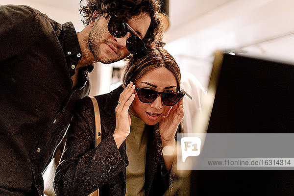 Lächelnde Frau probiert mit Freundin im Geschäft eine modische Sonnenbrille aus