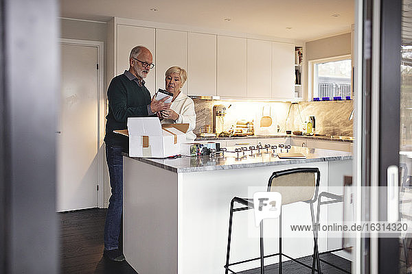 Älterer Mann in voller Länge nach Partner packt Paket über Kücheninsel aus