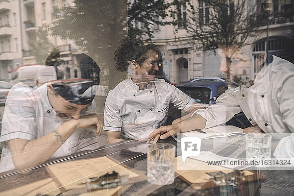 Glückliche Mitarbeiter sitzen am Restauranttisch durch Glasfenster gesehen