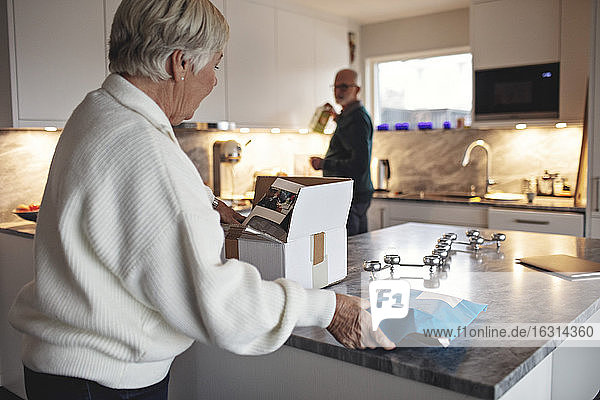 Side view of senior woman unpacking box over kitchen island