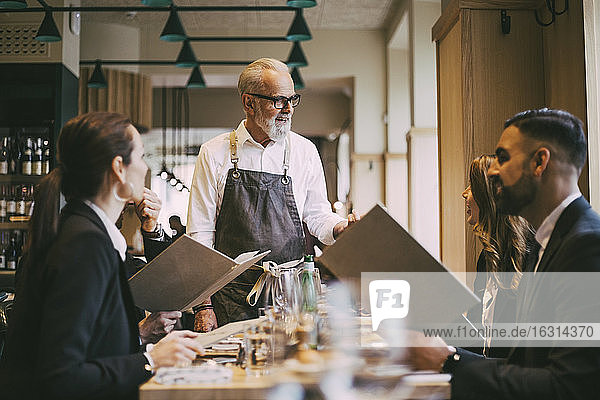 Waiter talking to business people while standing by table in restaurant
