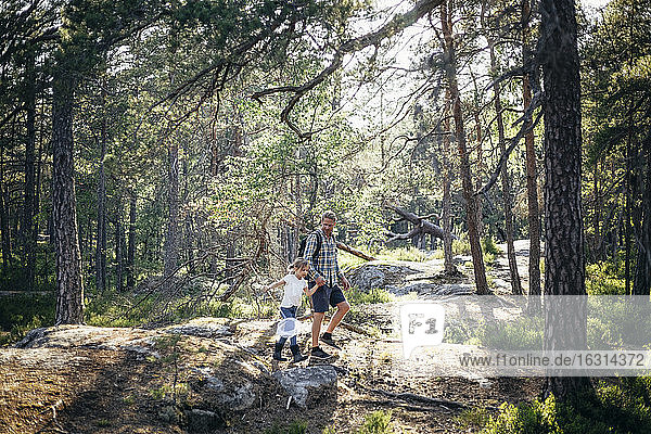 Daughter with fishing net walking while holding father's hand in forest
