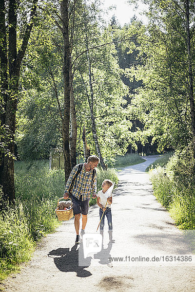 Daughter talking to father holding picnic basket on road in forest