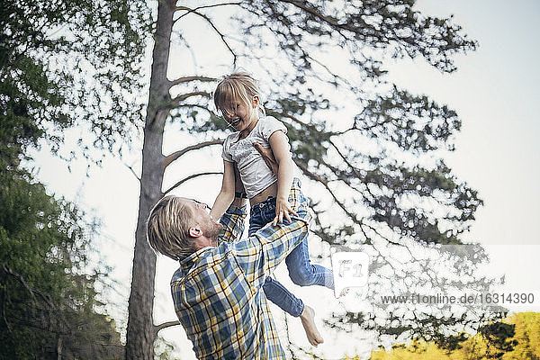 Glücklicher Vater hält Tochter in der Luft gegen Bäume