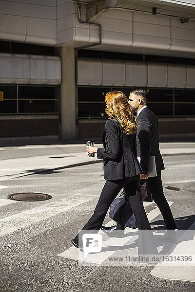 Seitenansicht einer Geschäftsfrau und eines Geschäftsmannes beim Überqueren einer Straße in der Stadt