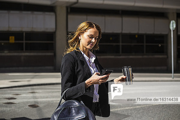 Businesswoman with smart phone crossing road in city