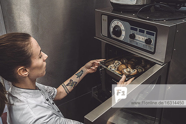 Hochwinkelansicht einer Köchin beim Backen von Pilzen im Ofen