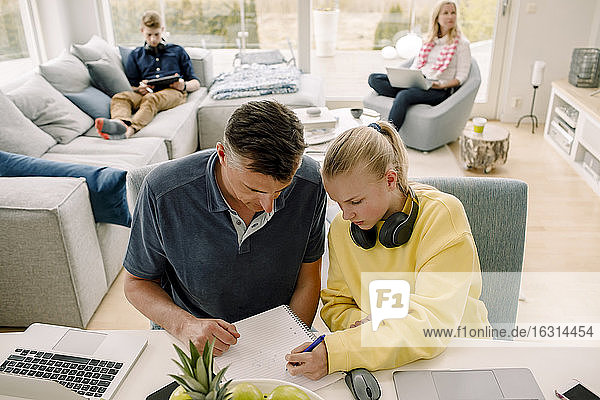 Hochwinkelaufnahme eines Vaters  der seine Tochter unterrichtet  während er im Wohnzimmer am Tisch sitzt